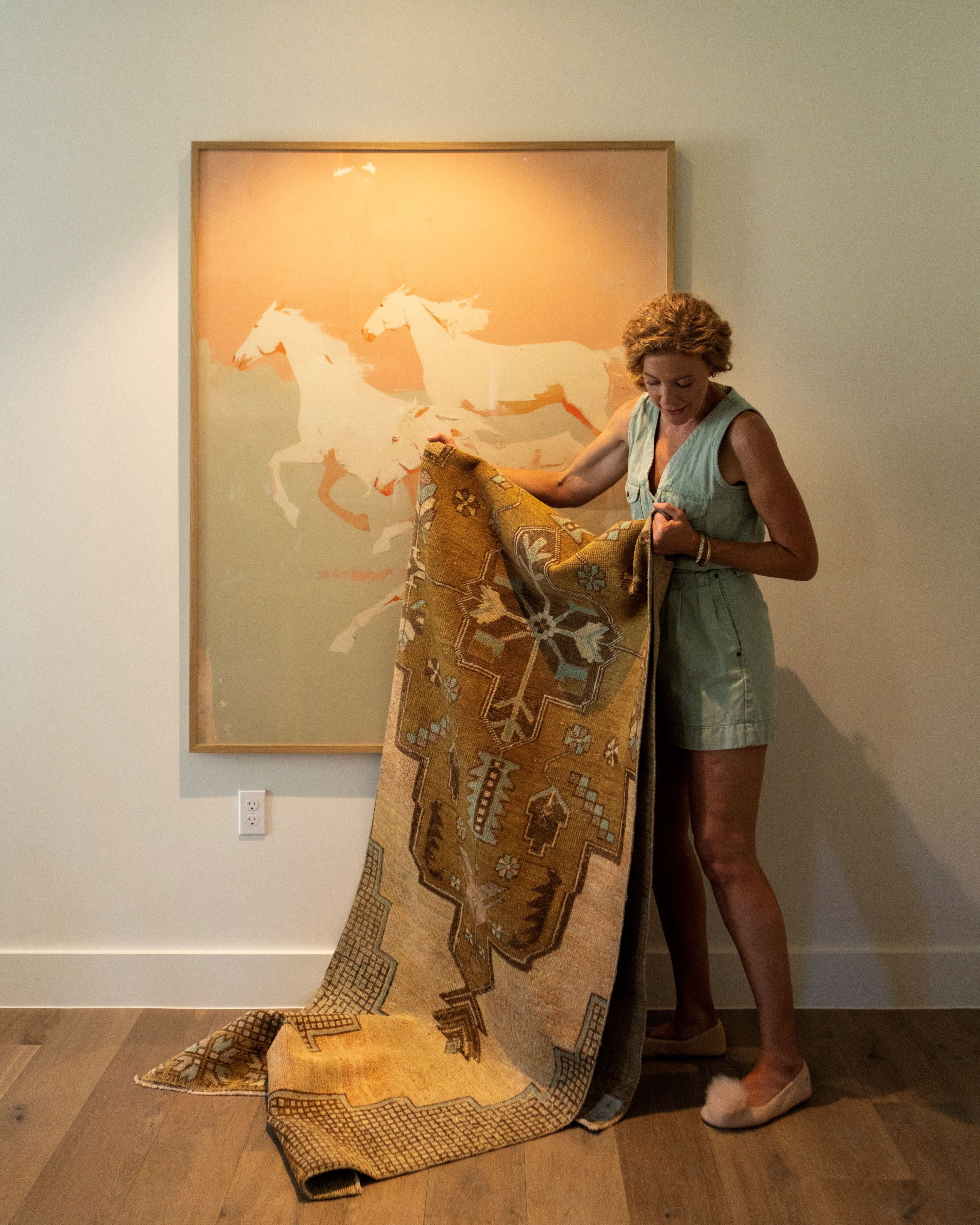 Woman holding a large decorative blanket with horse design in front of a wall with a similar artwork.